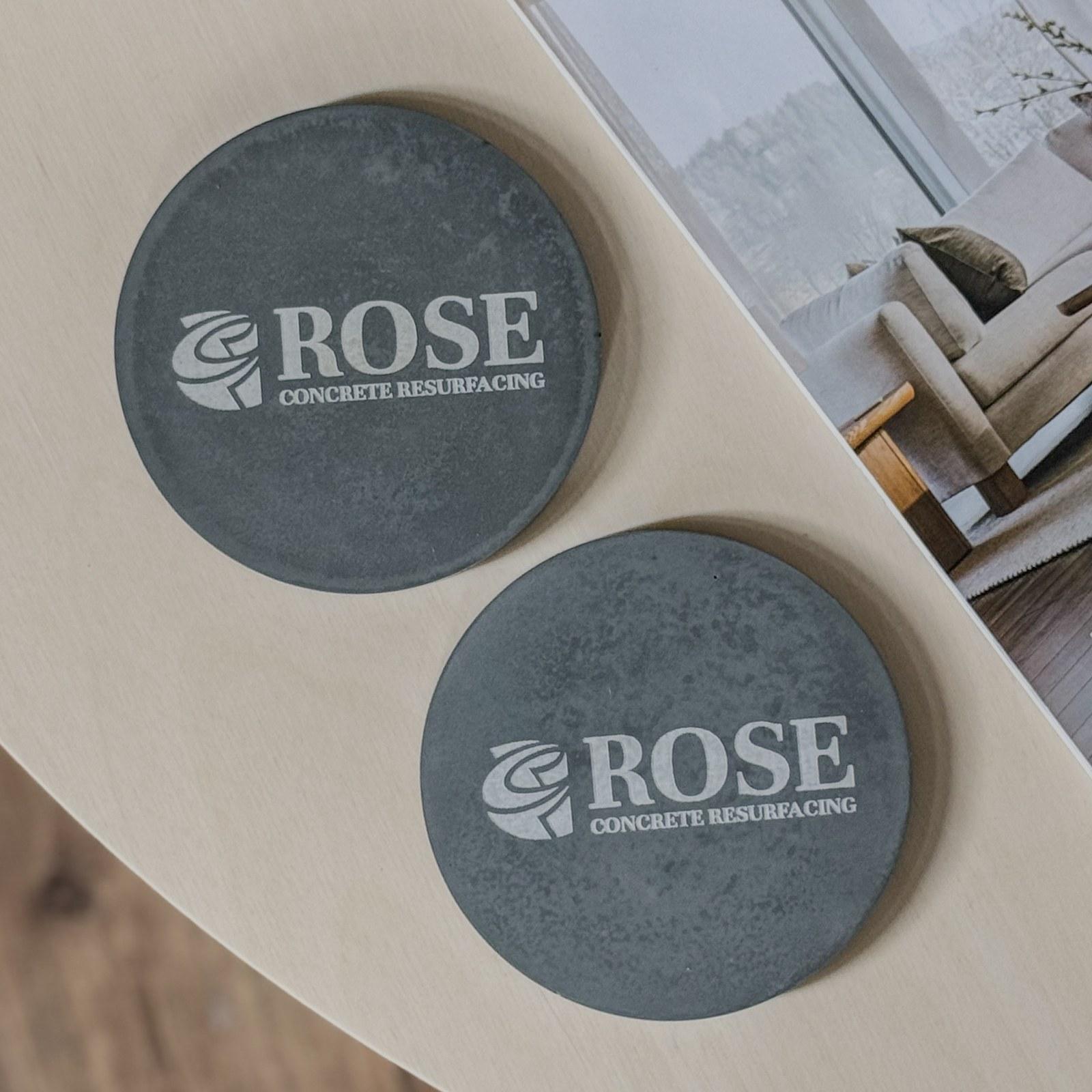 Dark grey round concrete coasters engraved with the Rose Concrete Resurfacing logo