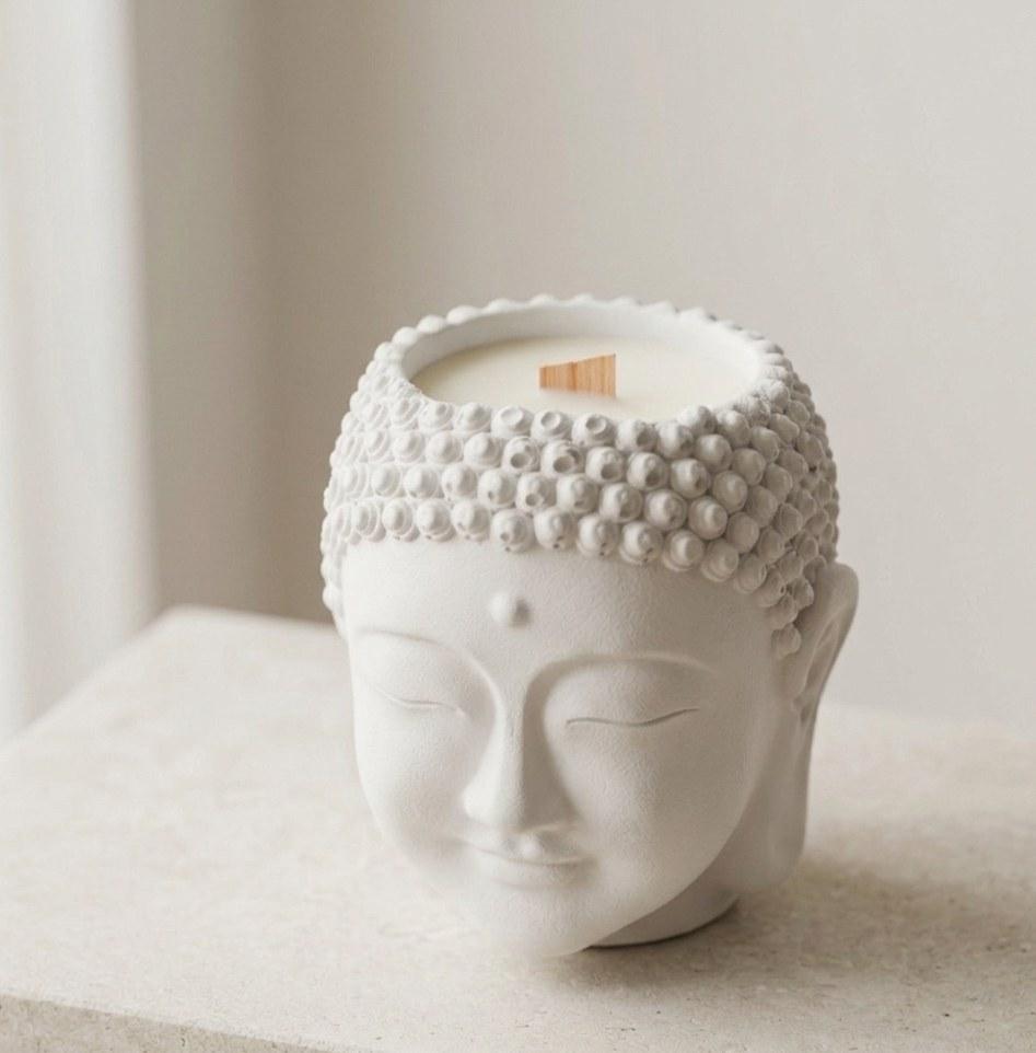 Sculpted Buddha head candle with a wood wick on a stone shelf