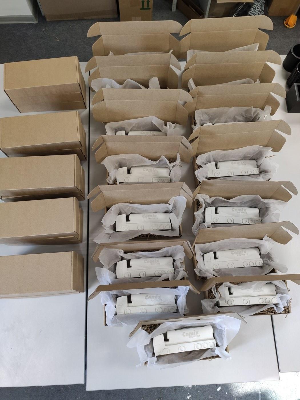 Batch of white concrete Cemix trucks packed into individual kraft gift boxes with tissue paper at the JOS Factory studio