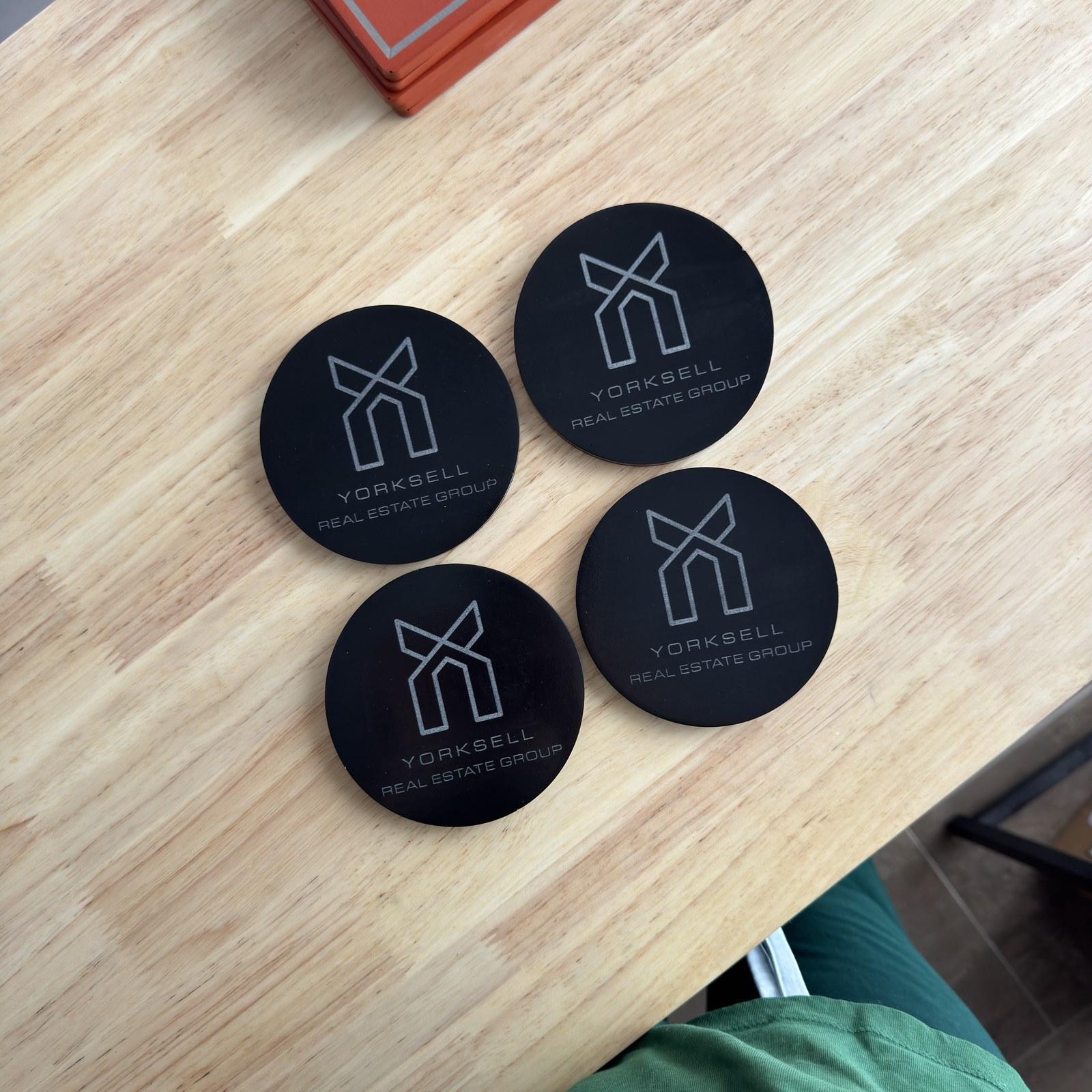 Round black concrete coasters with an engraved real estate group logo