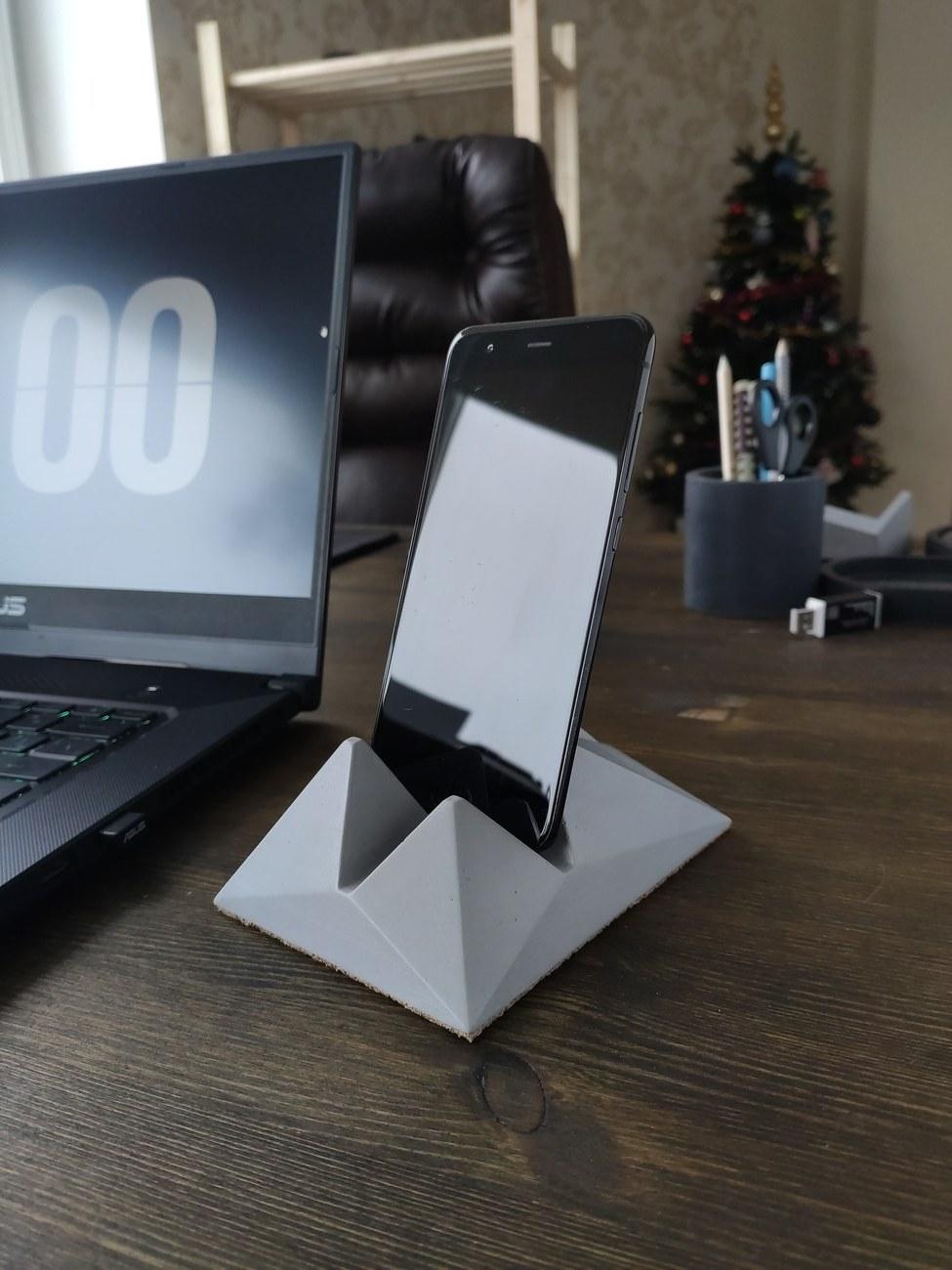 Concrete phone holder in use on a desk beside a laptop, with a Christmas tree in the background