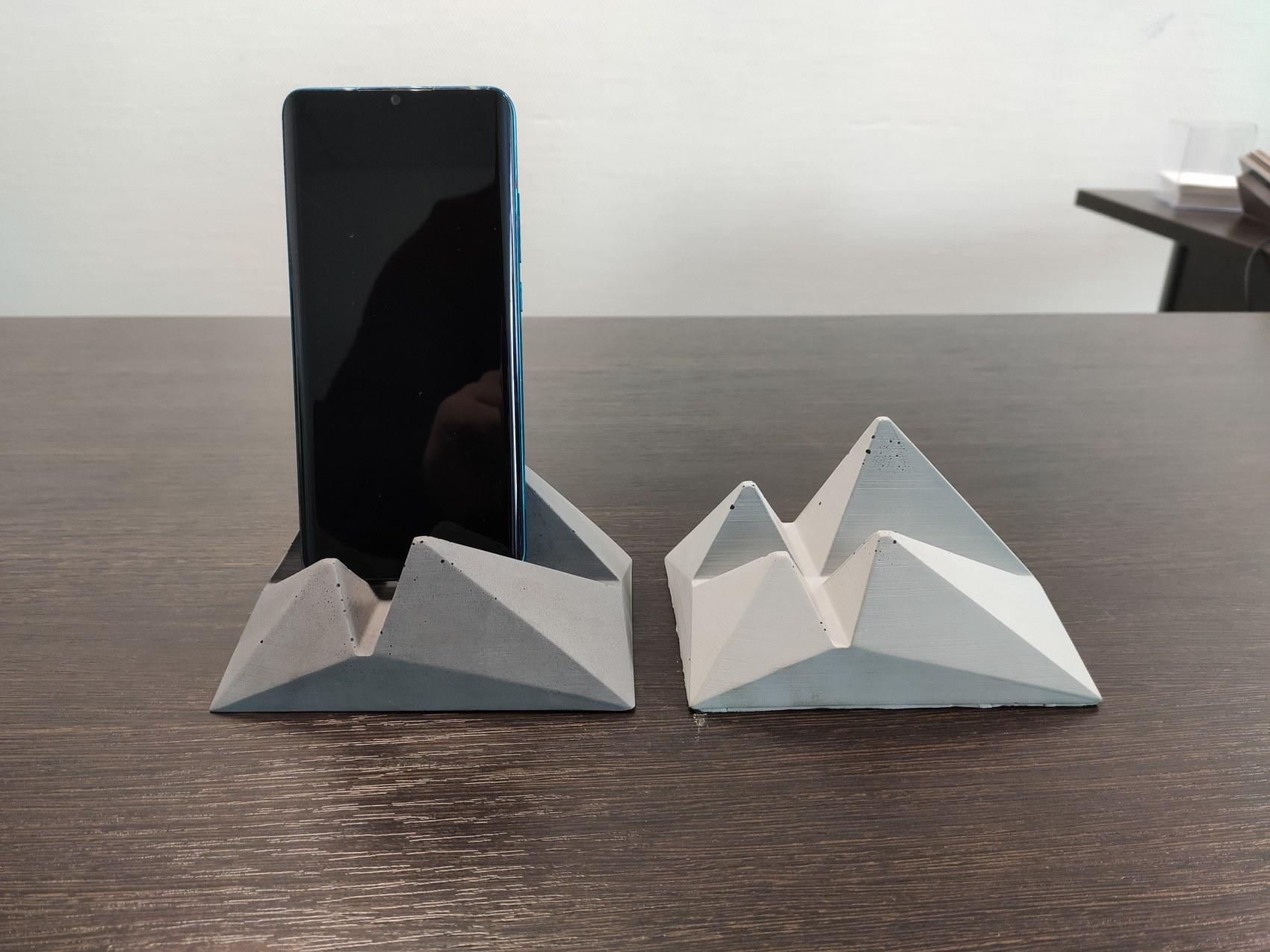 Two concrete mountain-range phone holders, one holding a phone